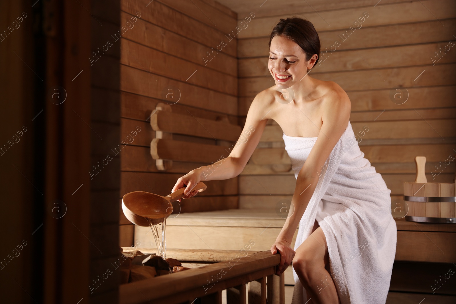 Photo of Smiling woman pouring water onto stones in sauna