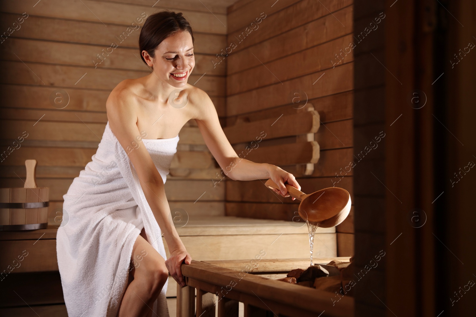 Photo of Smiling woman pouring water onto stones in sauna