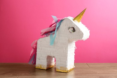 Photo of Beautiful pinata in shape of unicorn on wooden table against pink background