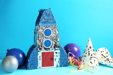 Photo of Beautiful pinata in shape of rocket, party cones and balloons on blue background