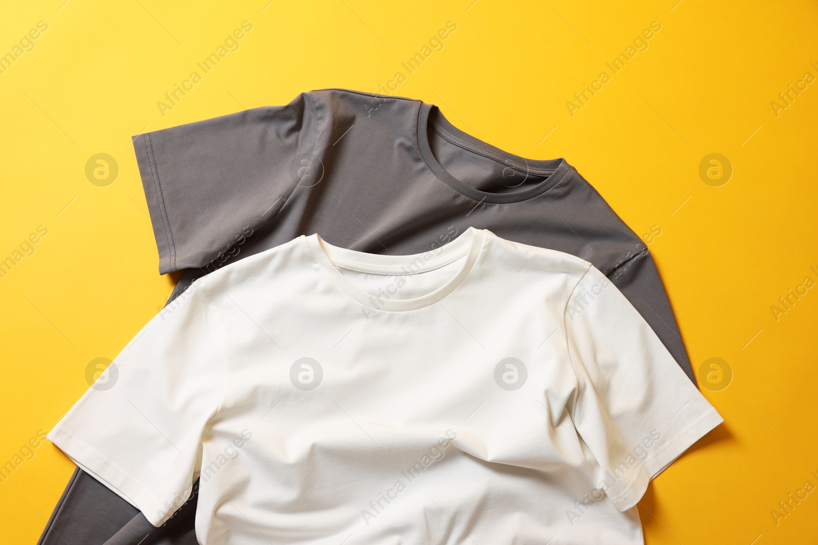 Photo of Blank t-shirts on yellow background, flat lay. Mockup for design