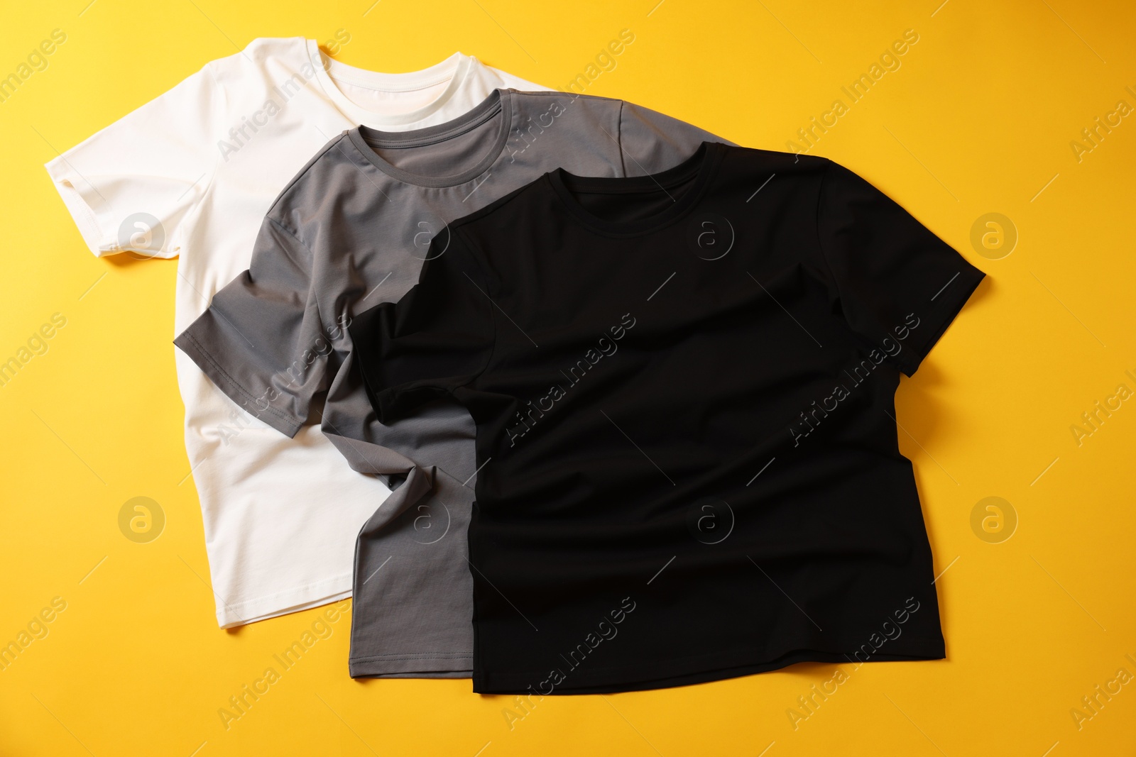 Photo of Blank t-shirts on yellow background, flat lay. Mockup for design