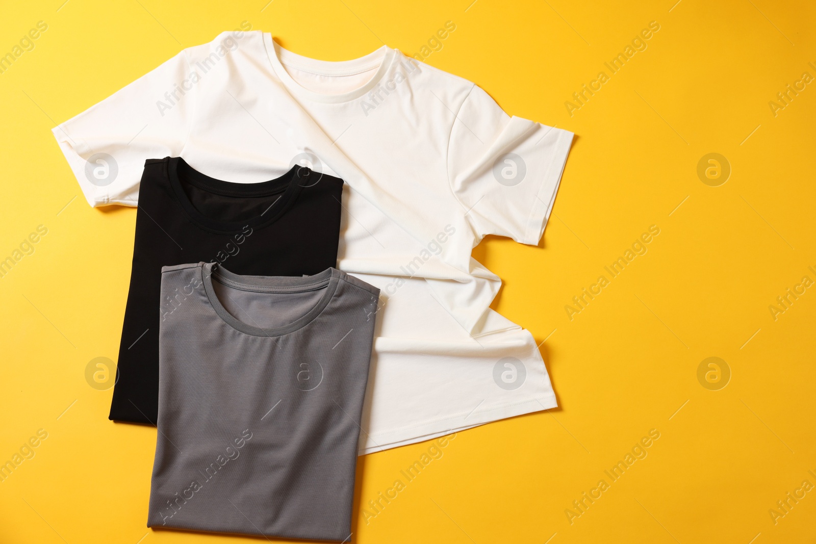 Photo of Blank t-shirts on yellow background, flat lay. Mockup for design