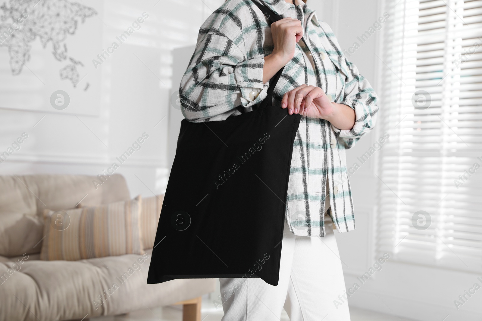 Photo of Woman with blank black shopper bag indoors, closeup. Mockup for design