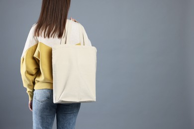 Woman with blank shopper bag on grey background, back view. Mockup for design