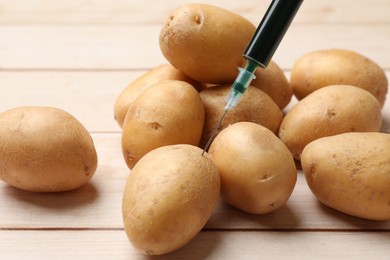 Photo of GMO concept. Injecting potato with syringe at wooden table, closeup