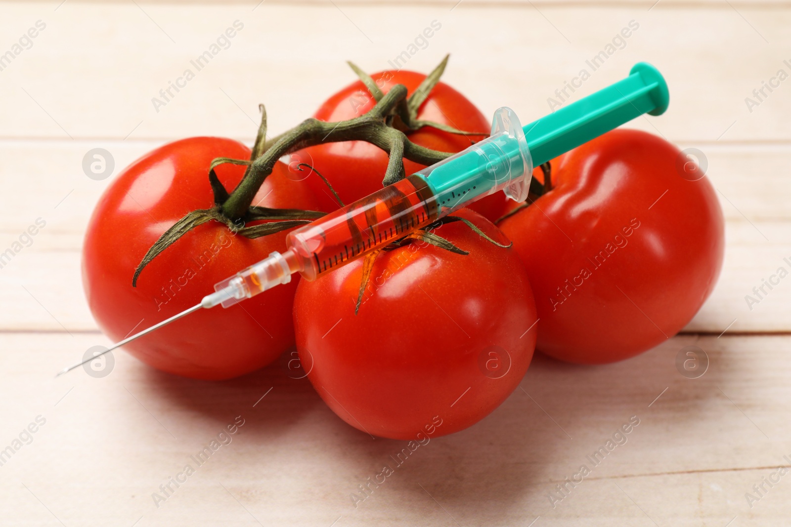 Photo of GMO concept. Fresh tomatoes and syringe on wooden table, closeup