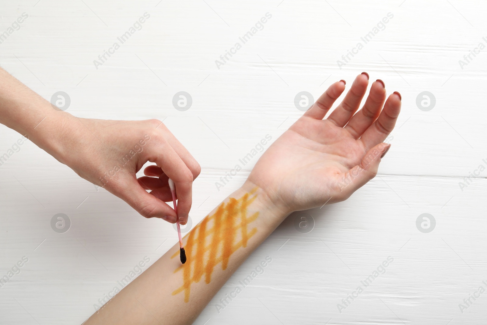 Photo of Woman applying topical iodine with cotton swab on hand at white wooden table, top view