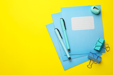 Photo of Stack of copybooks, binders, pens and sharpener on yellow background, flat lay. Space for text