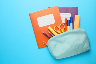 Photo of Colorful copybooks and pencil case with school stationery on light blue background, flat lay. Space for text