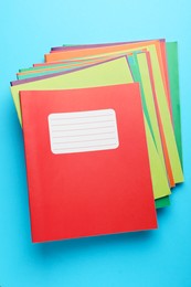 Photo of Stack of colorful copybooks on light blue background, top view. School stationery