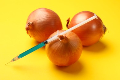 Photo of GMO concept. Onion bulbs and syringe with liquid on yellow background, closeup