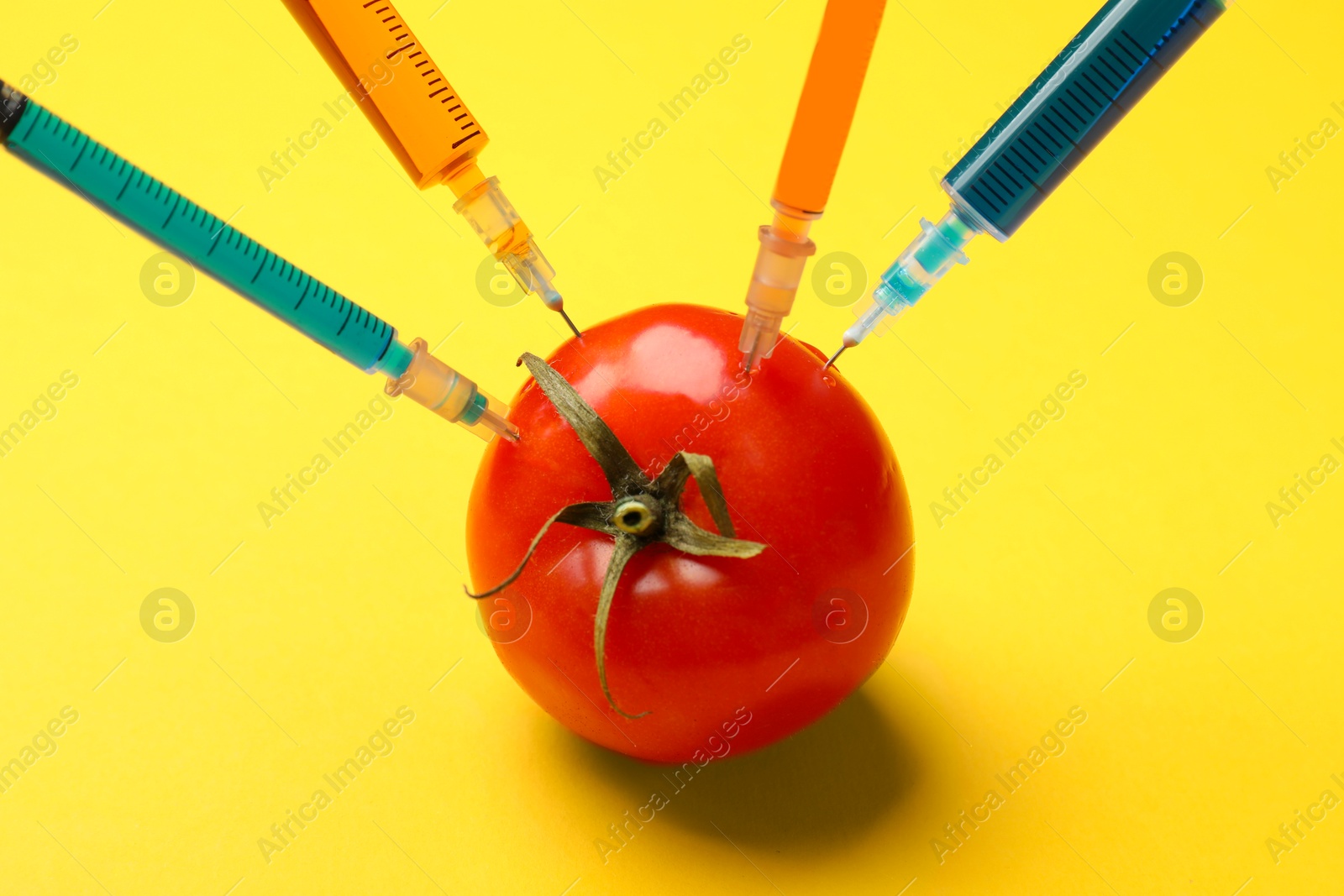 Photo of GMO concept. Tomato with different syringes on yellow background, closeup