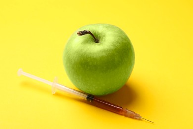 Photo of GMO concept. Green apple and syringe with liquid on yellow background, closeup