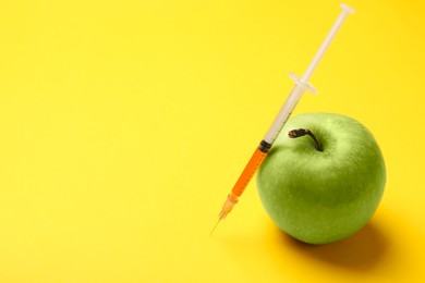 Photo of GMO concept. Green apple and syringe with liquid on yellow background, closeup. Space for text