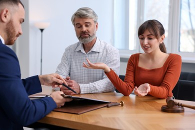 Photo of Couple having meeting with professional notary at wooden desk indoors