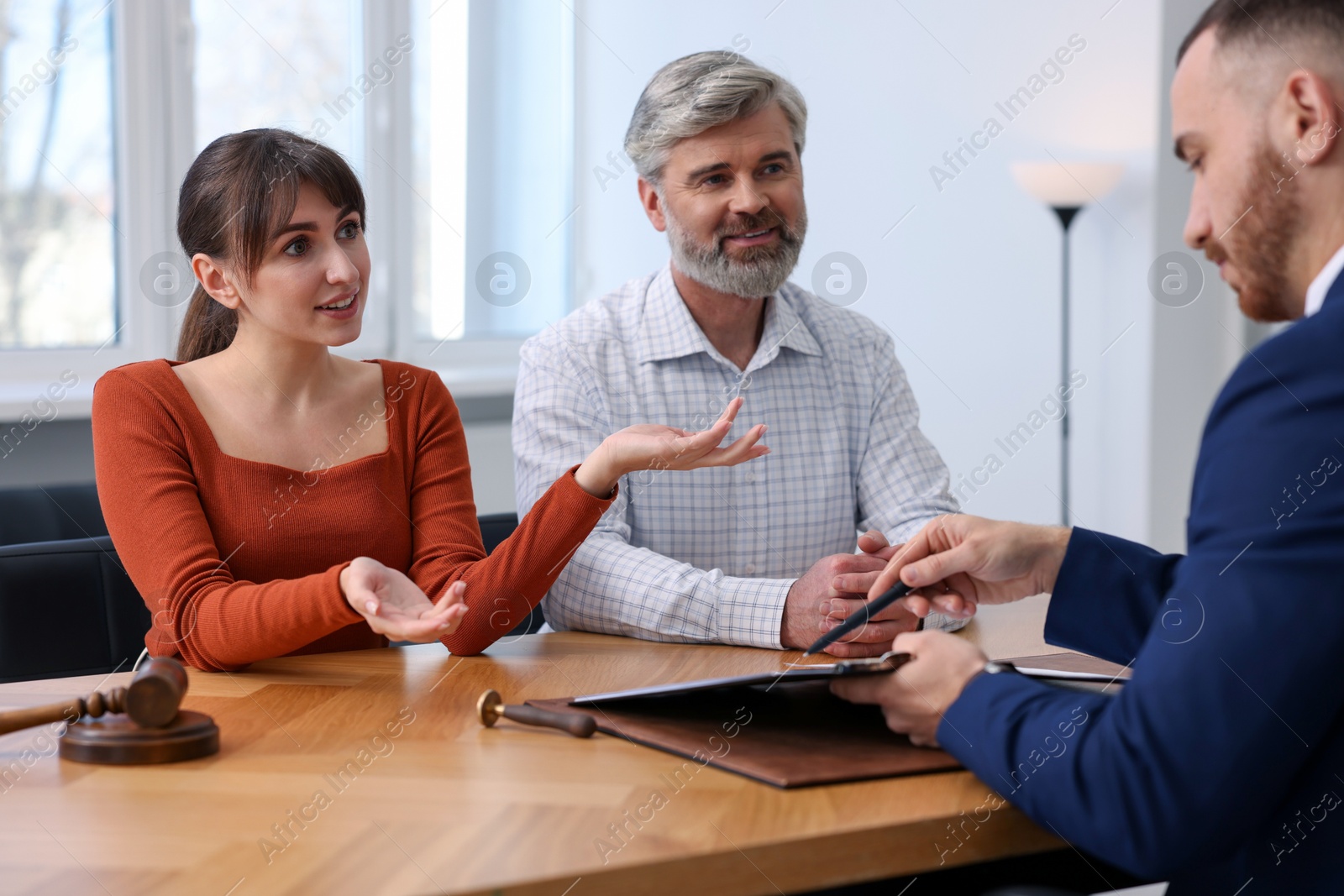 Photo of Couple having meeting with professional notary at wooden desk indoors