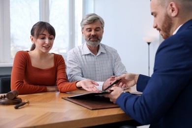 Photo of Couple having meeting with professional notary at wooden desk indoors