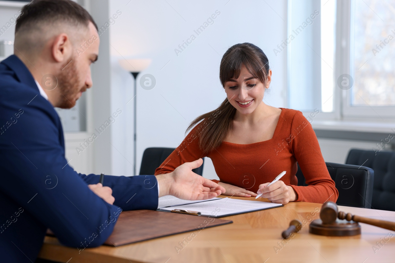 Photo of Client signing notarial paperwork during meeting with lawyer at wooden desk indoors