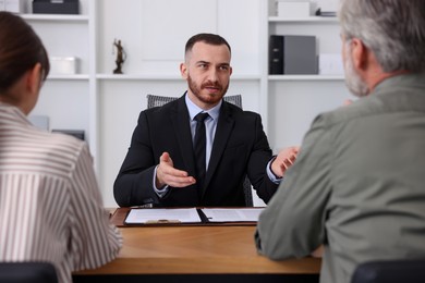 Man and woman having meeting with professional lawyer at wooden desk indoors