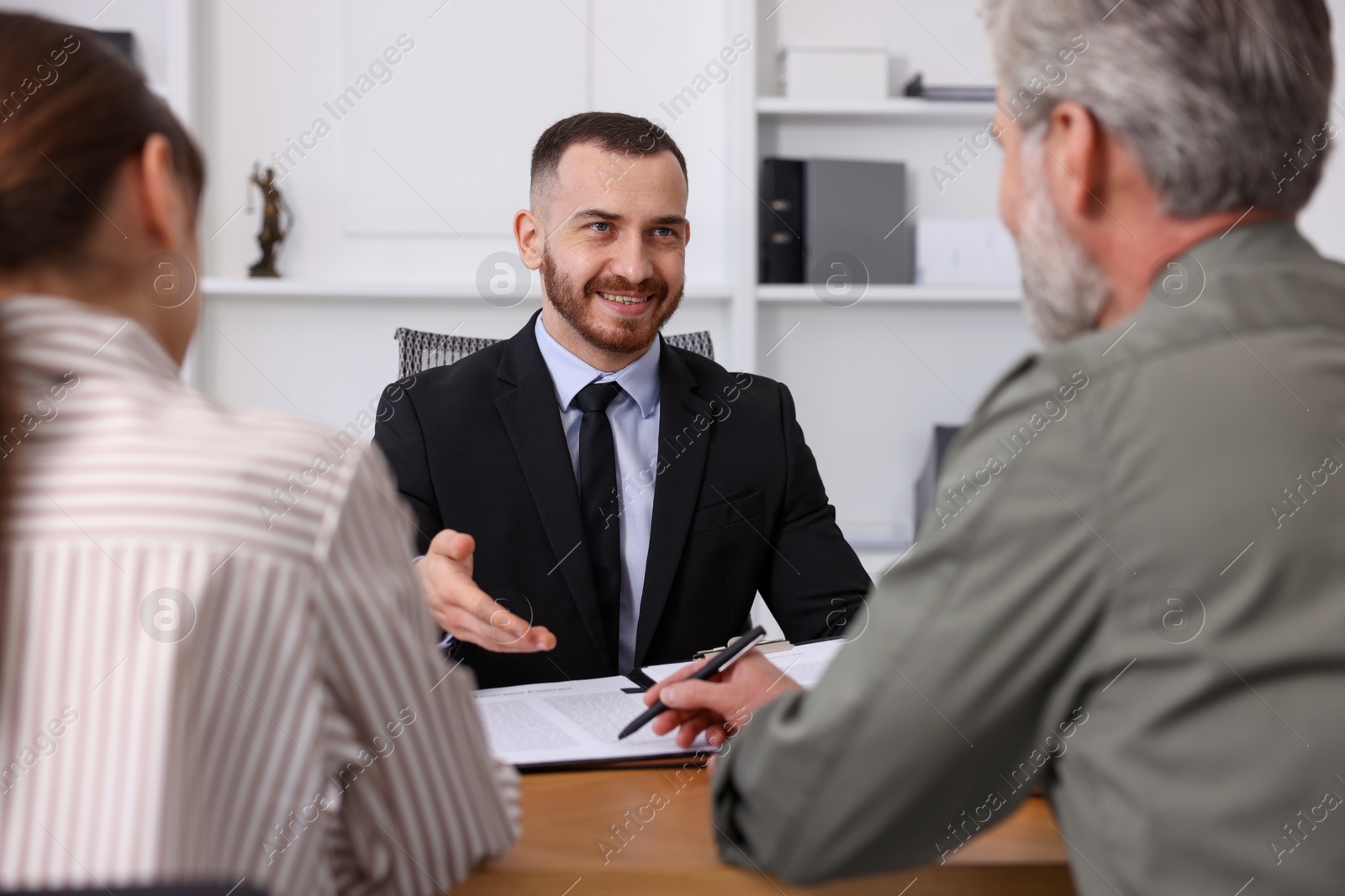 Photo of Clients signing notarial paperwork during meeting with lawyer at wooden desk indoors