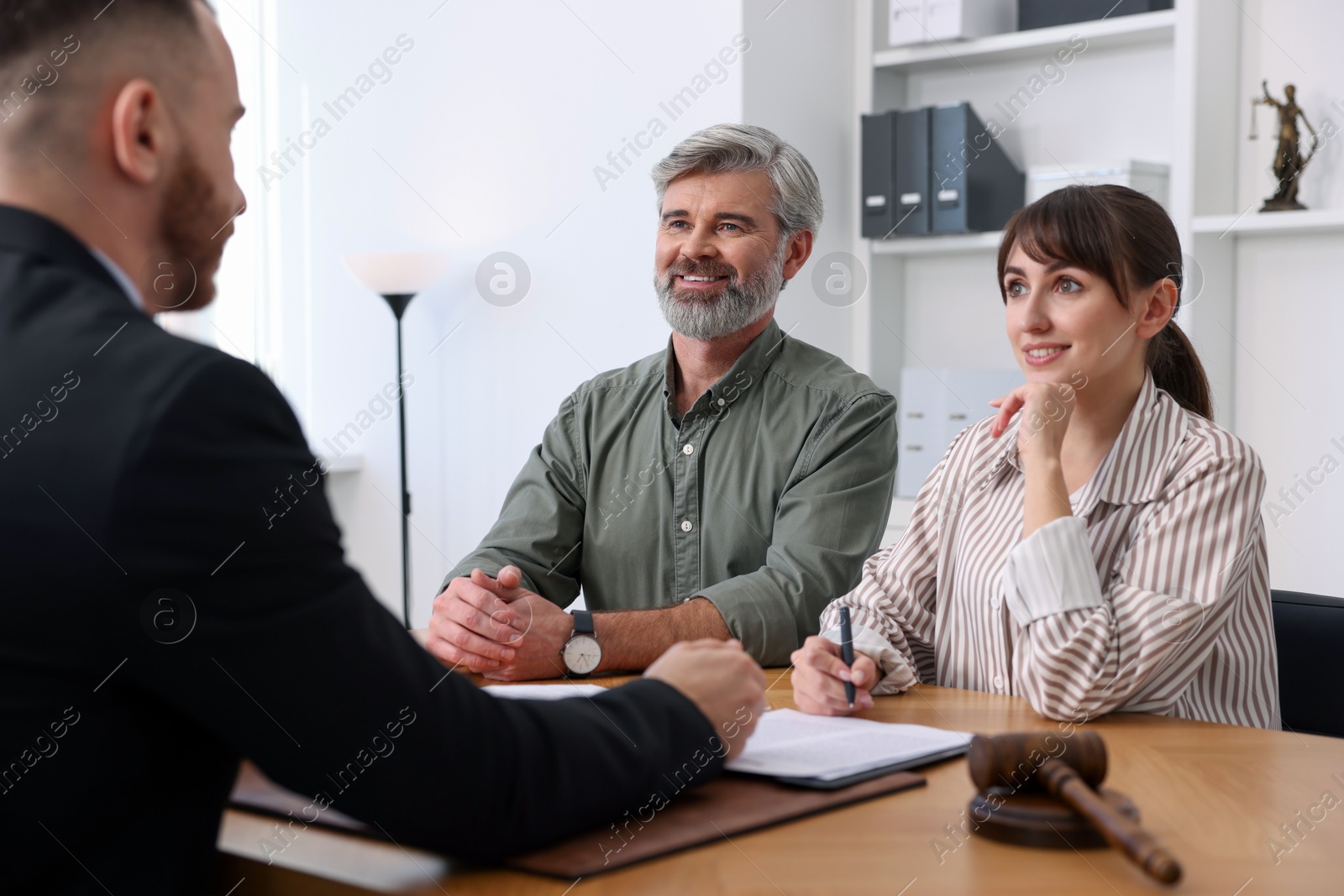 Photo of Clients signing notarial paperwork during meeting with lawyer at wooden desk indoors