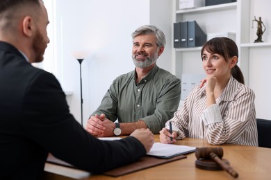 Clients signing notarial paperwork during meeting with lawyer at wooden desk indoors