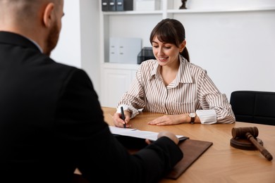 Woman having meeting with professional notary at wooden desk indoors