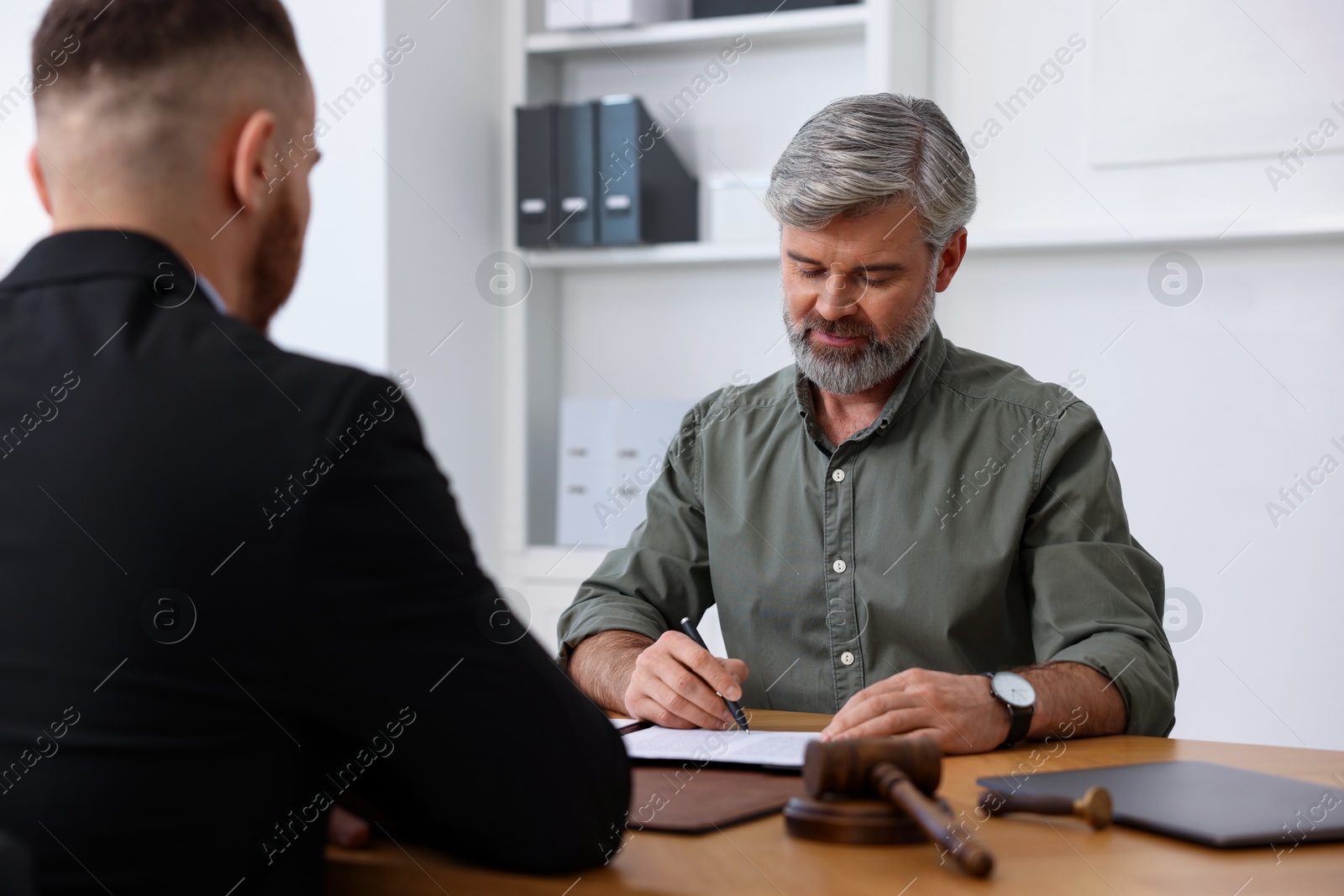 Photo of Client signing notarial paperwork during meeting with lawyer at wooden desk indoors