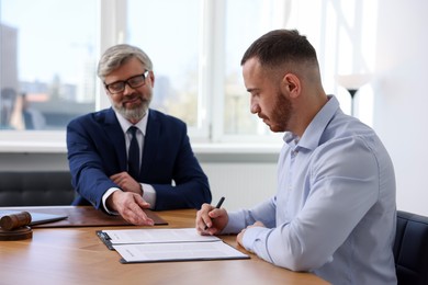 Photo of Client signing notarial paperwork during meeting with lawyer at wooden desk indoors, selective focus