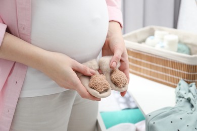 Photo of Pregnant woman with baby socks at home, closeup