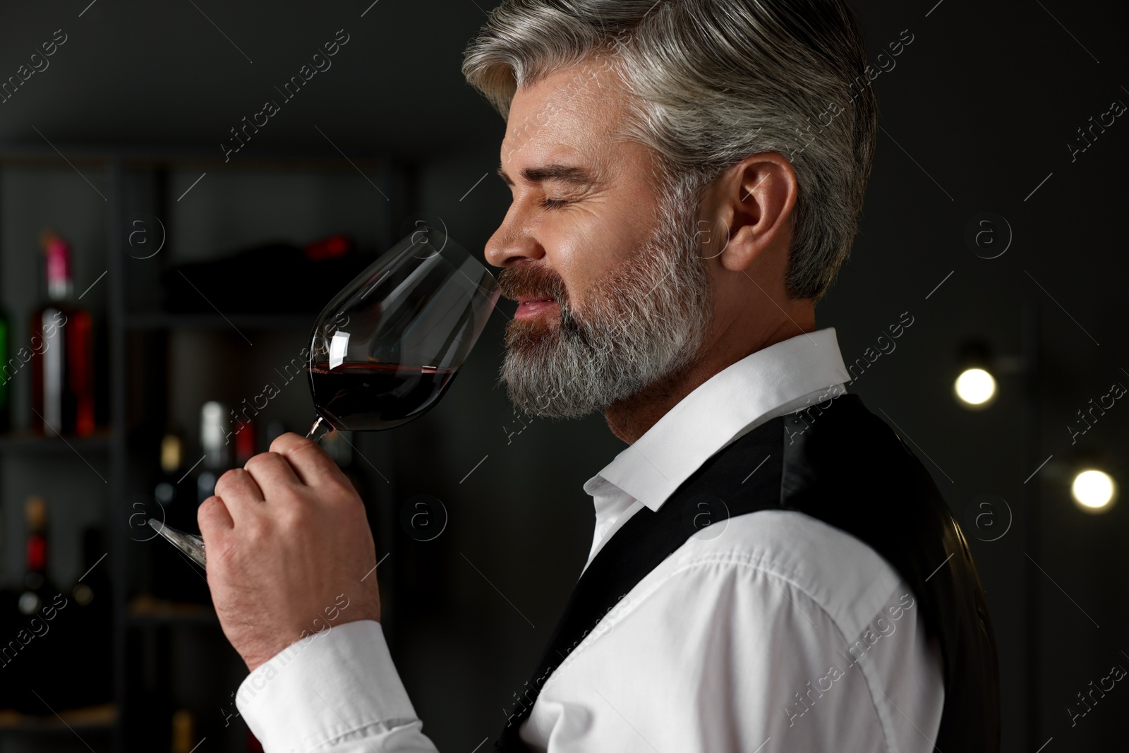 Photo of Professional sommelier tasting red wine in glass indoors