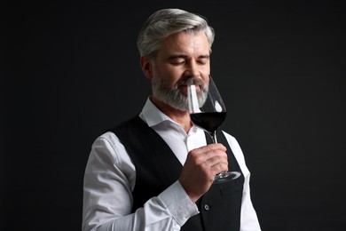 Professional sommelier tasting red wine on black background