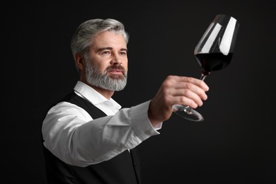 Professional sommelier analyzing quality of red wine on black background