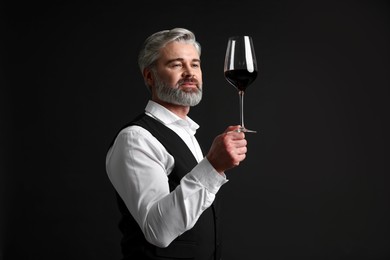 Photo of Professional sommelier analyzing quality of red wine on black background