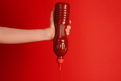 Photo of Woman squeezing ketchup out of bottle on red background, closeup