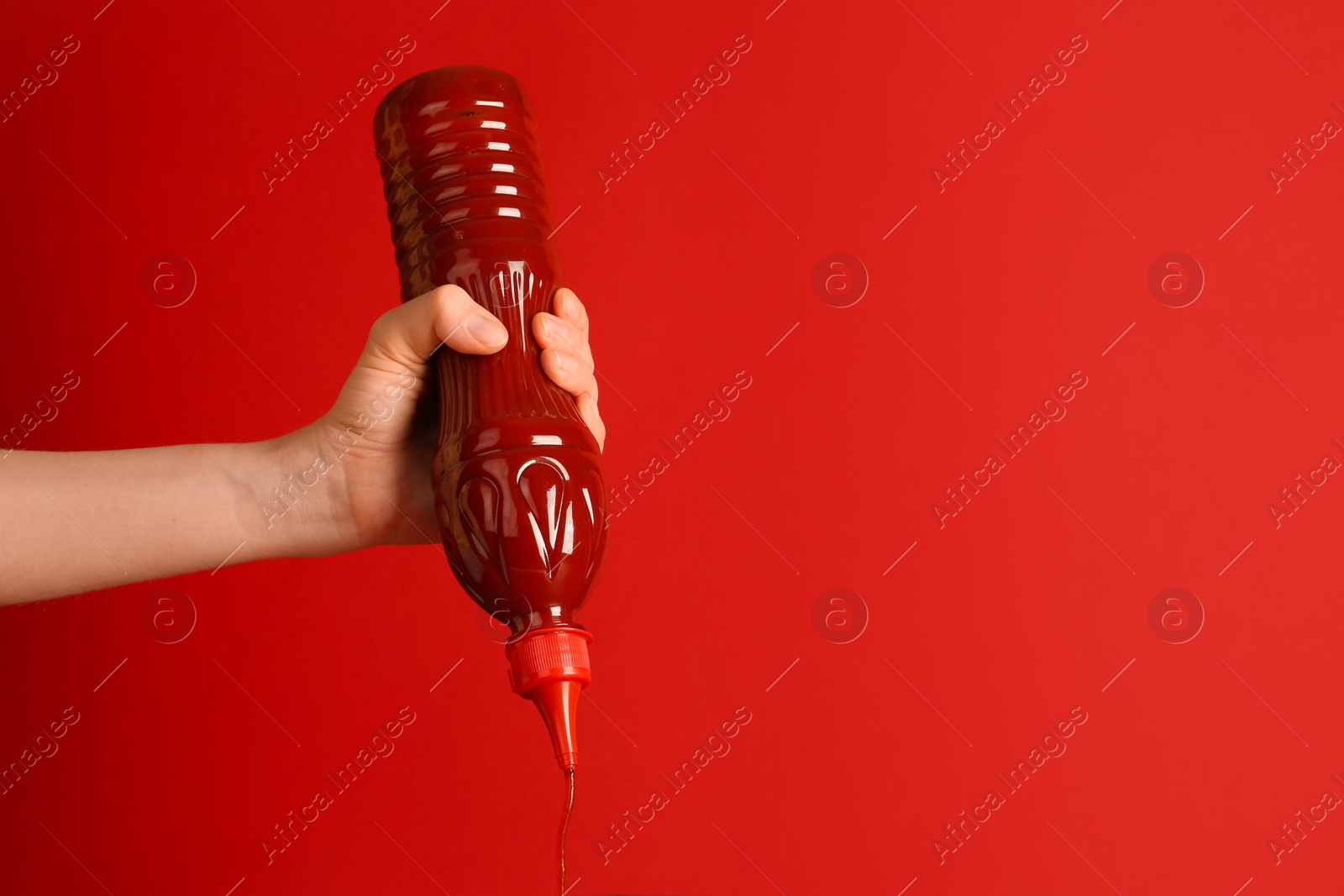 Photo of Woman squeezing ketchup out of bottle on red background, closeup. Space for text