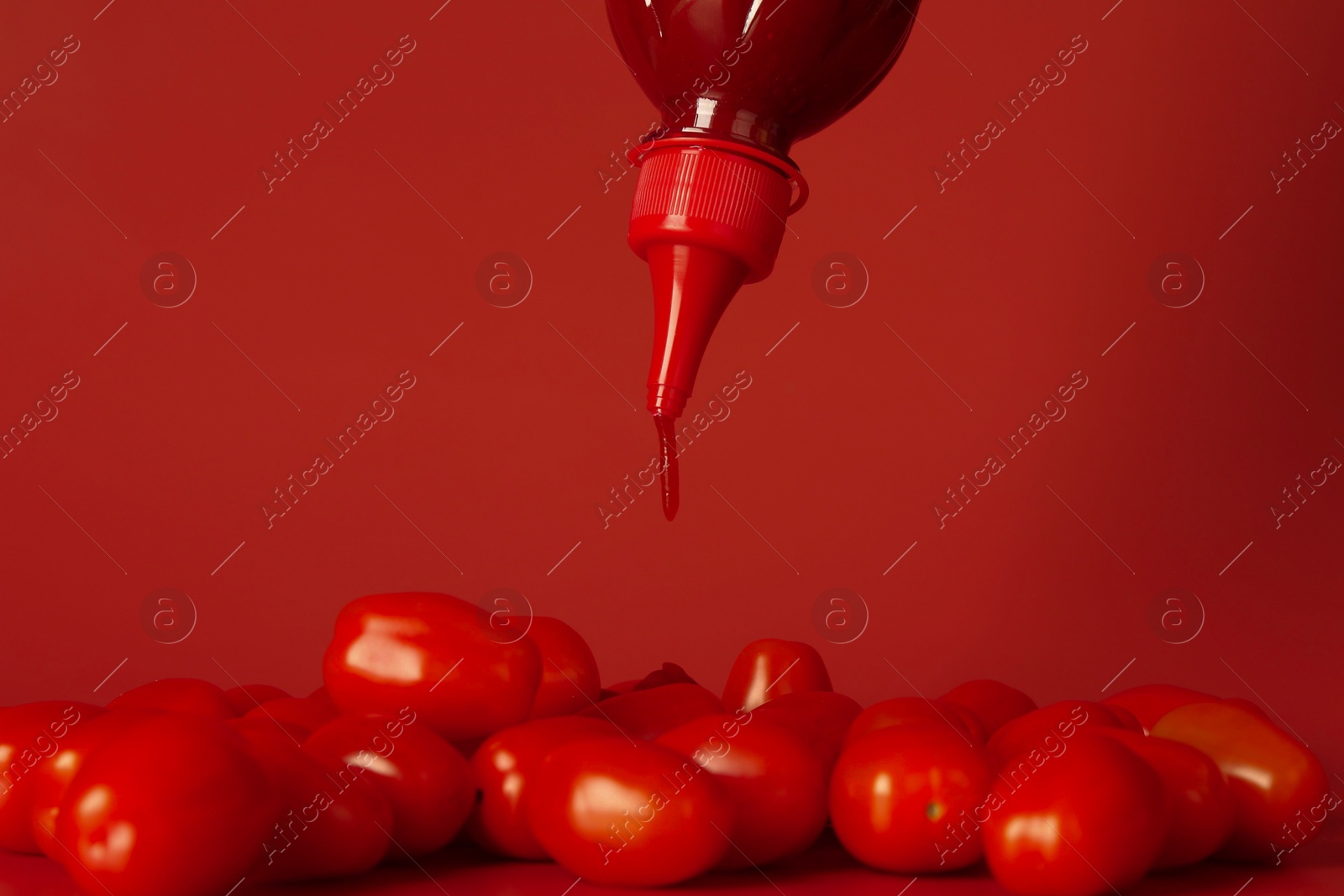 Photo of Squeezing ketchup from bottle over tomatoes on red background, closeup