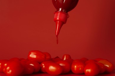 Photo of Squeezing ketchup from bottle over tomatoes on red background, closeup