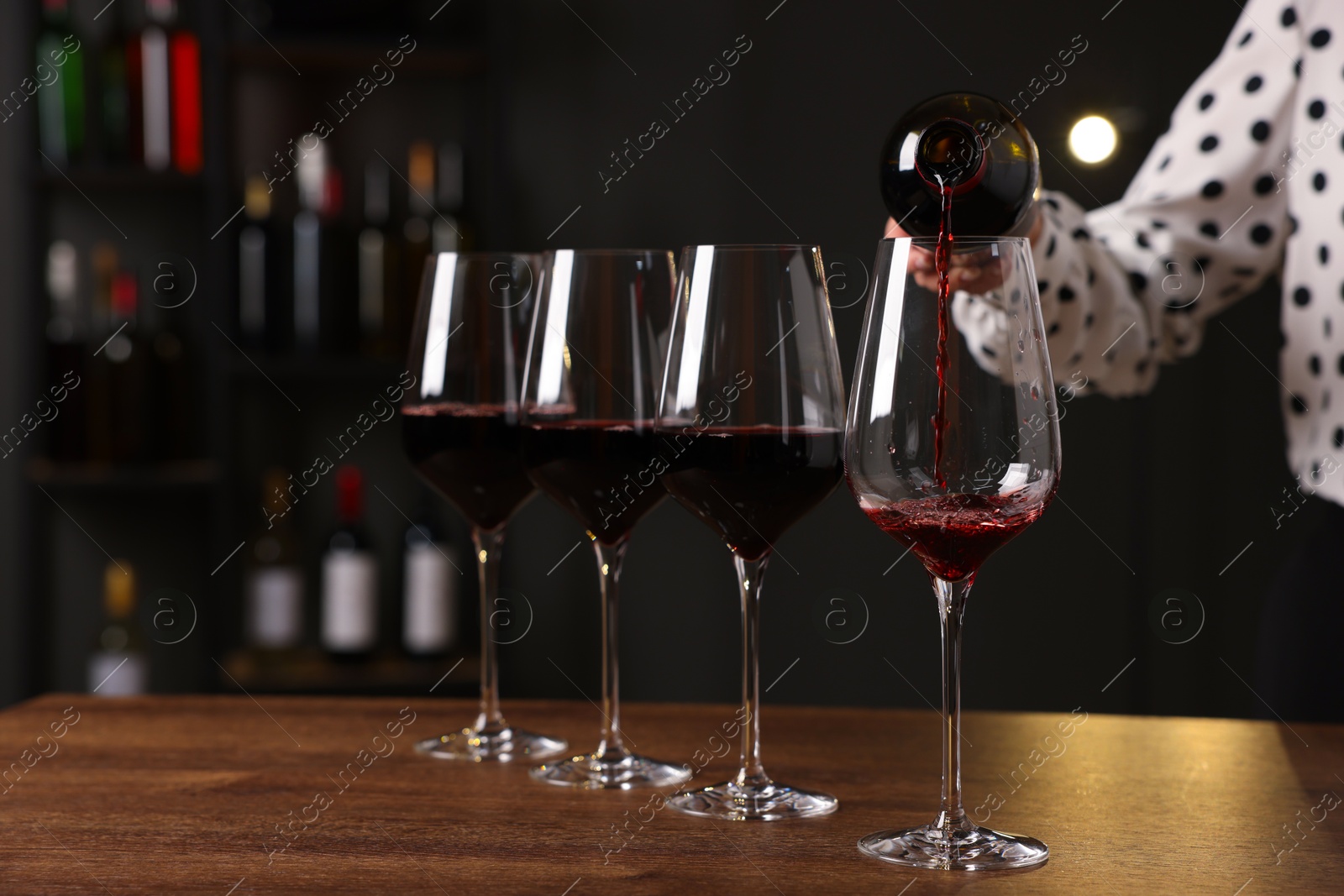 Photo of Professional sommelier pouring red wine into glasses at wooden table indoors, closeup