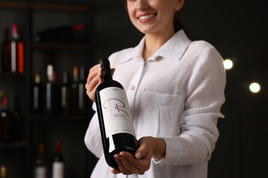 Photo of Professional sommelier holding bottle of red wine indoors, closeup