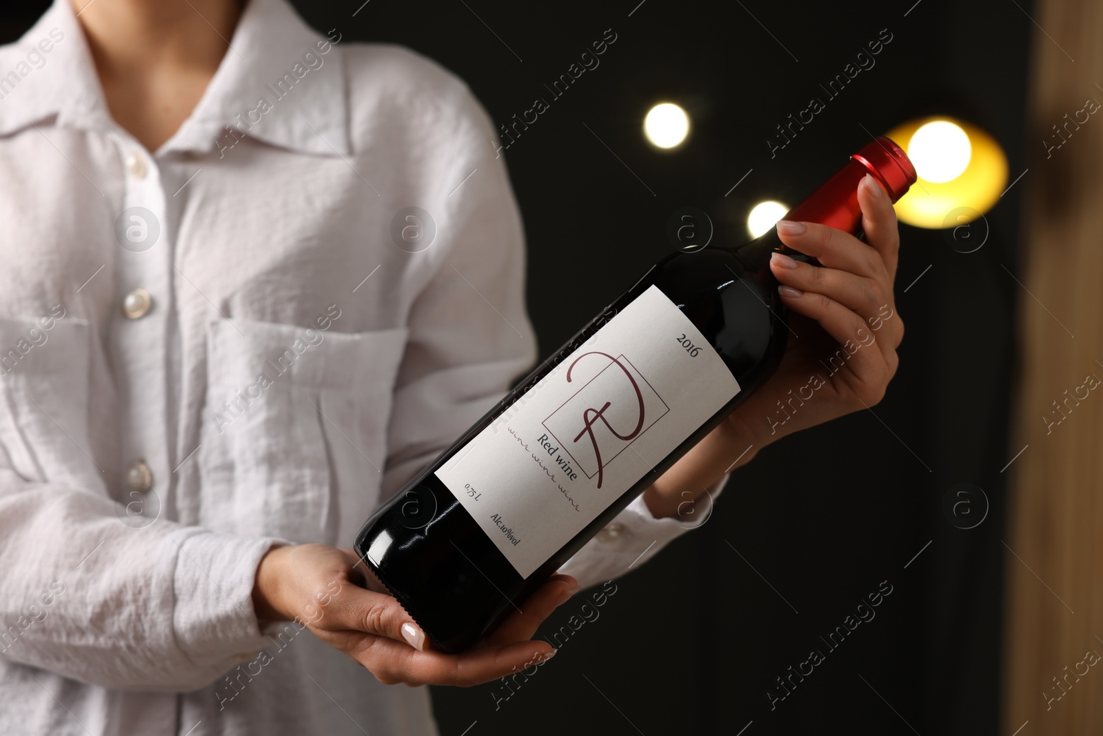 Photo of Professional sommelier holding bottle of red wine indoors, closeup