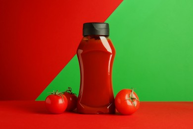 Photo of Bottle of ketchup and tomatoes on color background