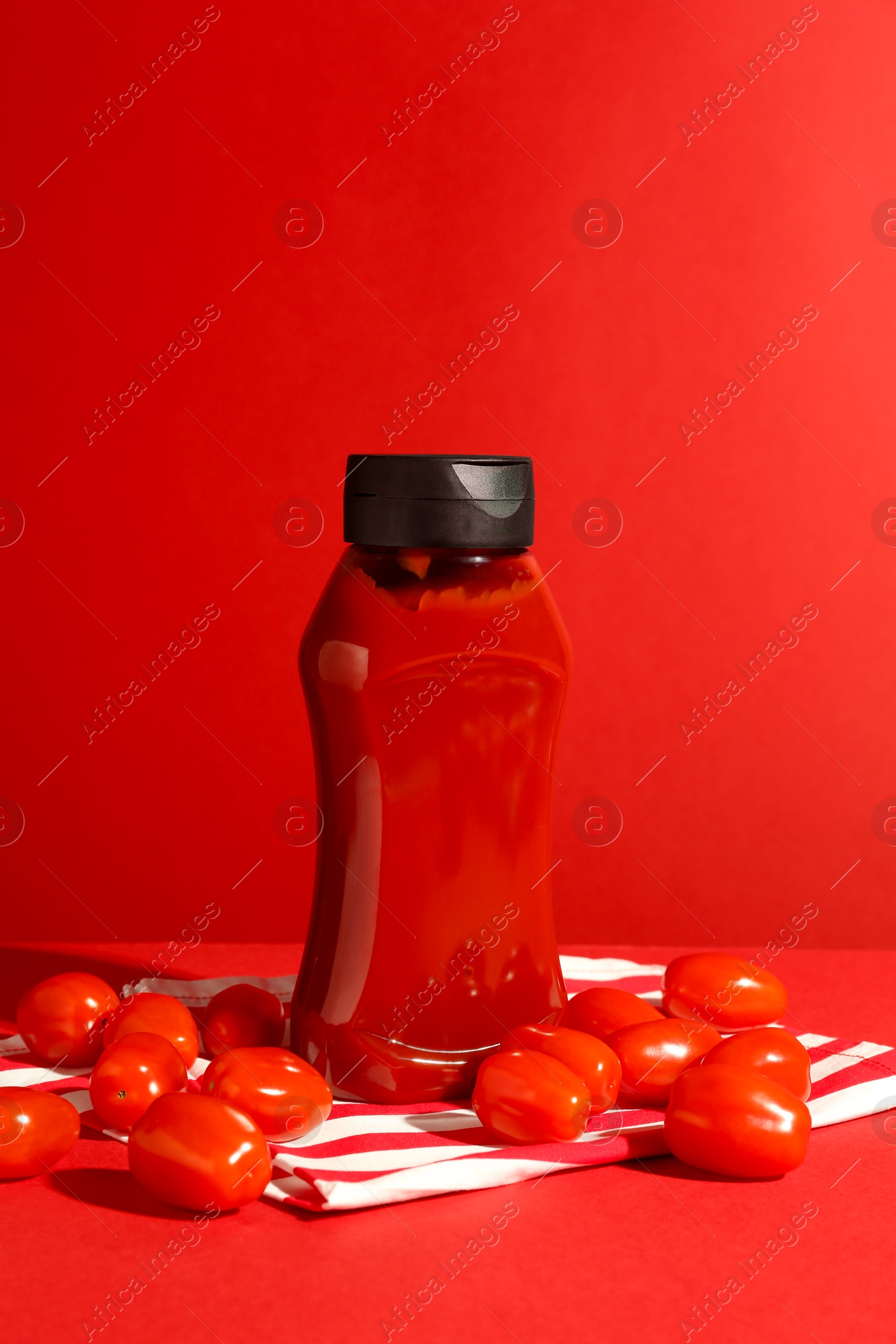 Photo of Bottle of ketchup and tomatoes on red background