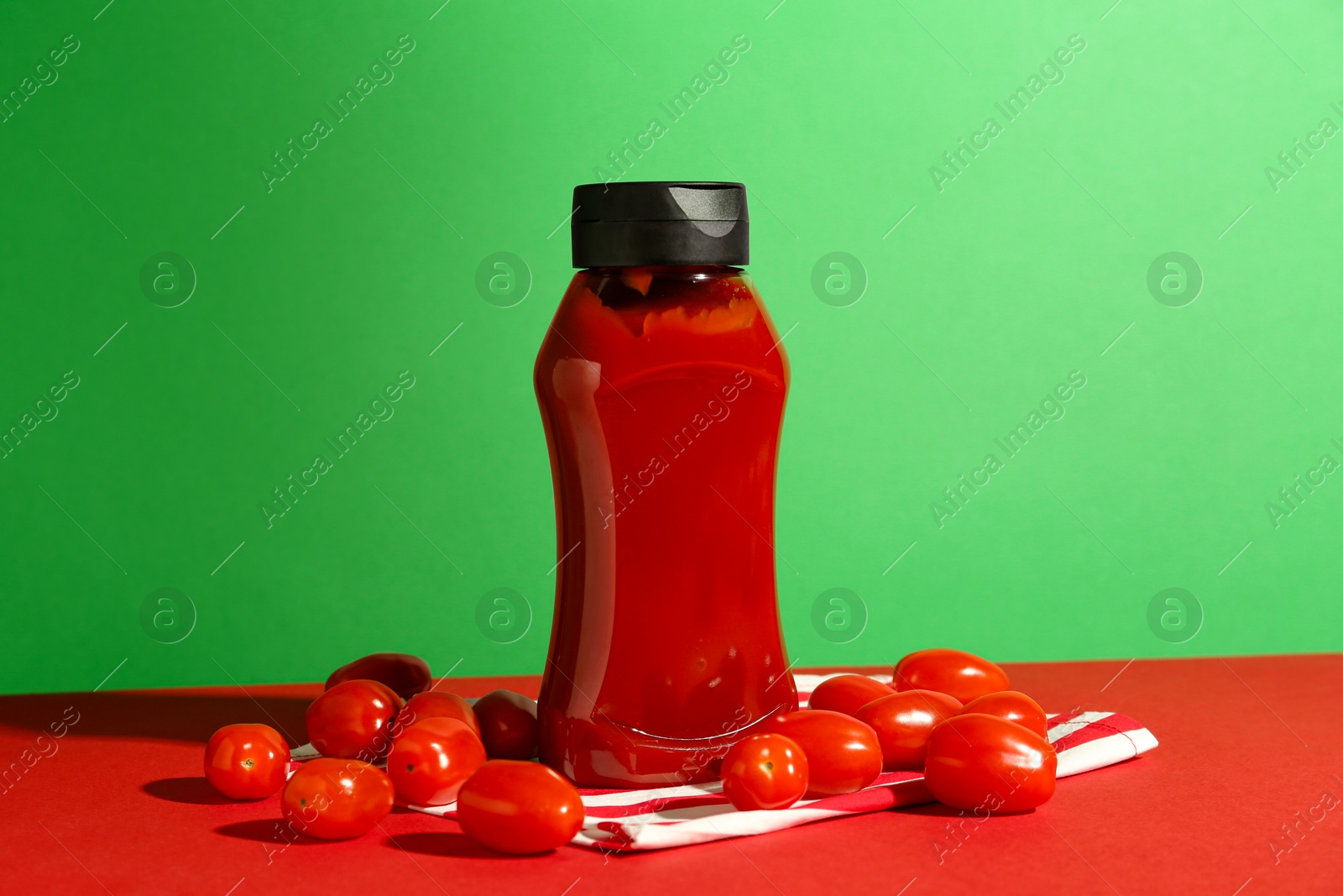 Photo of Bottle of ketchup and tomatoes on color background