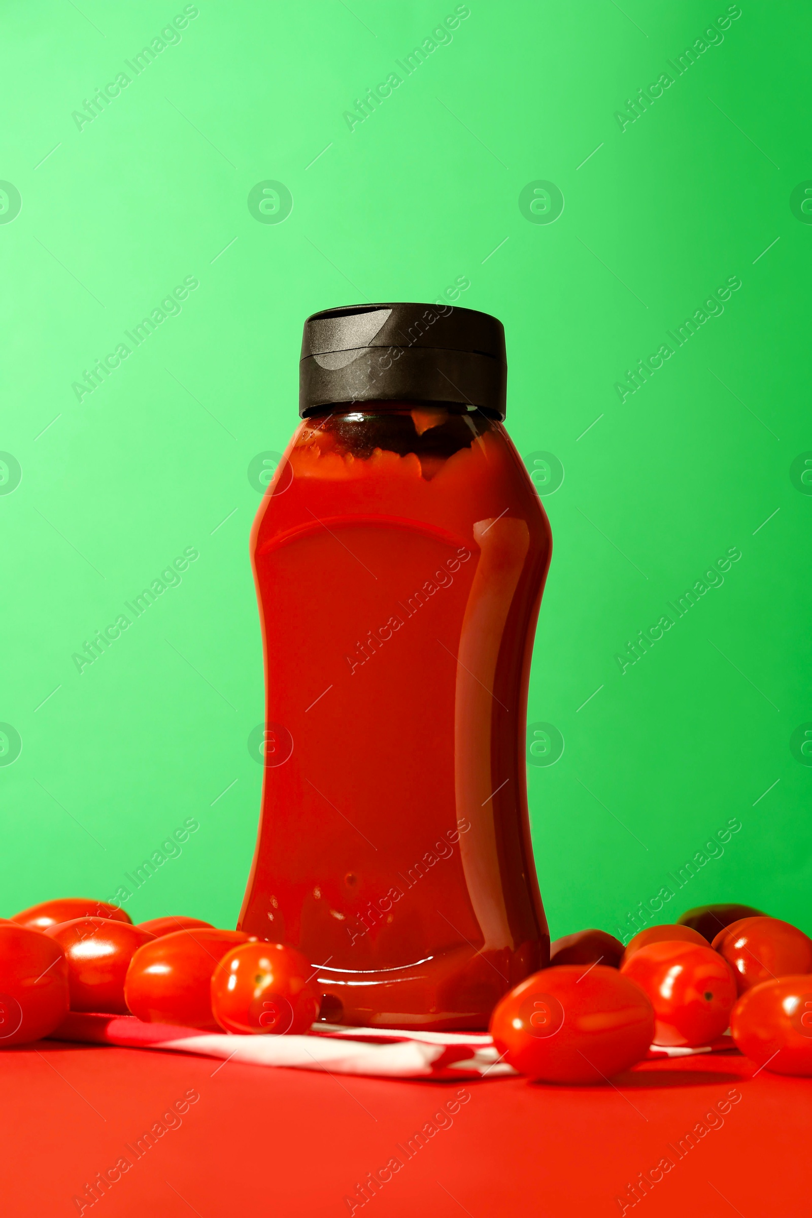 Photo of Bottle of ketchup and tomatoes on color background