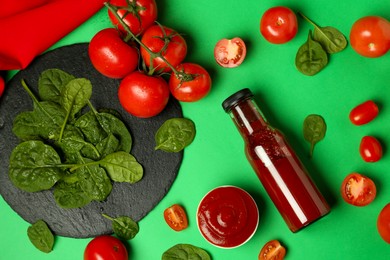 Photo of Ketchup, tomatoes and spinach on green background, flat lay