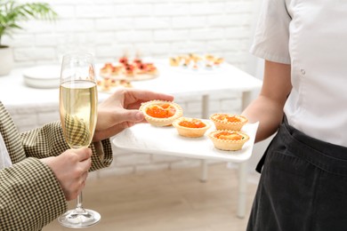 Photo of Woman taking tasty canape from waiter with board indoors, closeup