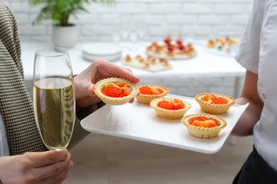 Photo of Woman taking tasty canape from waiter with board indoors, closeup