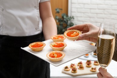 Photo of Woman taking tasty canape from waiter with board indoors, closeup